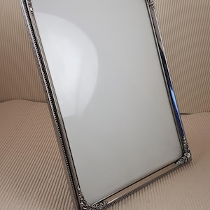 May include: A silver picture frame with an ornate design. The frame is empty and ready for a photo.