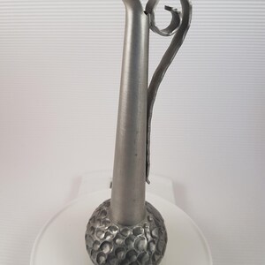 K&ouml;nnte beinhalten: Eine silberne Metallvase mit einem strukturierten, runden Boden und einem langen, schlanken Hals. Die Vase hat einen einzigartigen, gekr&auml;uselten Griff.