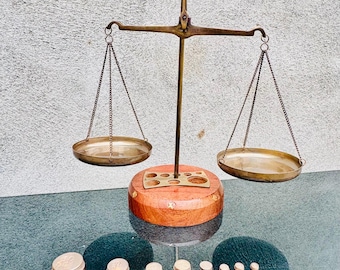 Puede incluir: Una balanza antigua de latón con dos platillos circulares suspendidos por cadenas. La balanza tiene una base de madera y está acompañada de un juego de pesas de latón de varios tamaños. Un artículo vintage, probablemente utilizado para medir.