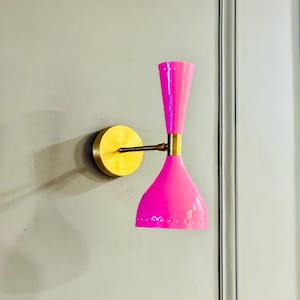 Puede incluir: Aplique de pared rosa brillante con base y brazo de latón. La lámpara tiene una pantalla cónica y una parte superior cilíndrica. El accesorio está montado sobre una placa redonda de latón. Diseño moderno de mediados de siglo.