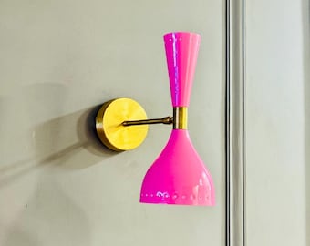 May include: A vibrant pink wall sconce featuring a brass base and arm. The sconce showcases a conical shade and a cylindrical top, mounted on a circular brass plate. The design is reminiscent of mid-century modern aesthetics.
