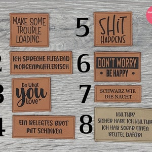 Könnte beinhalten: Acht braune Leder-Patches mit schwarzem Text. Die Patches zeigen verschiedene Sprüche, darunter "Make Some Trouble Loading...", "Do What You Love", "Shit Happens" und "Don't Worry, Be Happy".