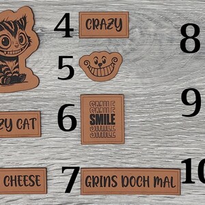Könnte beinhalten: Zehn braune Lederpatches mit schwarzem Text und Bildern. Die Patches zeigen verschiedene Designs, darunter eine Katze, ein lächelndes Gesicht und die Worte "Crazy Cat", "Say Cheese", "Grins Doch Mal", "Smile" und "We're all mad here".