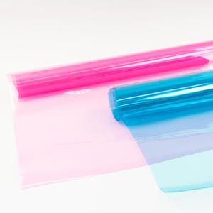 Könnte beinhalten: Zwei Rollen durchscheinendes Geschenkpapier, eine rosa und eine blaue, sind teilweise auf einer weißen Oberfläche abgewickelt.