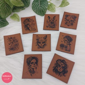 Könnte beinhalten: Zehn braune Lederpatches mit verschiedenen Designs. Die Designs beinhalten einen Schädel, eine Katze, ein Einhorn, einen Hund, eine Frau mit Blumen im Haar und ein Zitat über das Bewältigen des Sturms.