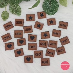Könnte beinhalten: Eine Sammlung brauner Holzetiketten mit verschiedenen Wörtern und Symbolen in Schwarz gedruckt. Die Wörter beinhalten "Liebe", "Sweet" und "Cool". Die Symbole beinhalten Herzen und Sterne.