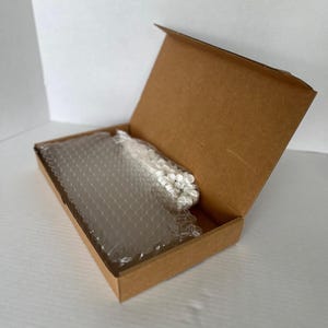 May include: A brown cardboard box with the lid open, revealing a wrapped item inside. The item is protected by bubble wrap and white packing material. The box is on a white surface.