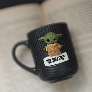 Pu&ograve; includere: Una tazza di ceramica bianca con manico nero e la scritta "But First, Coffee" in grassetto nero. La tazza &egrave; appoggiata su una superficie di legno. La tazza &egrave; alta circa 10 cm.