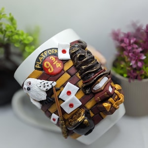 May include: White ceramic mug with a 3D design of a brick wall with the words "Platform 9 3/4" in gold lettering. The mug also features a white owl, a brown hat, a wand, and a stack of books.