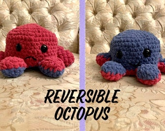 May include: A reversible crochet octopus in two color combinations: red and blue. One side shows a red octopus with a sad face, while the other side is blue with a happy face. The text "REVERSIBLE OCTOPUS" is below the octopuses.
