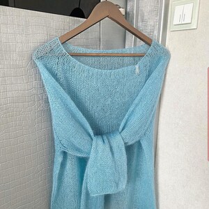 May include: A light blue knitted sweater with a loose fit and a wide neckline. The sweater is made of a soft, delicate yarn and has a slightly textured appearance.