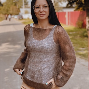 May include: A brown sheer knit sweater with long sleeves and a loose fit. The sweater has a subtle ombre effect, transitioning from a lighter brown at the top to a darker brown at the bottom.