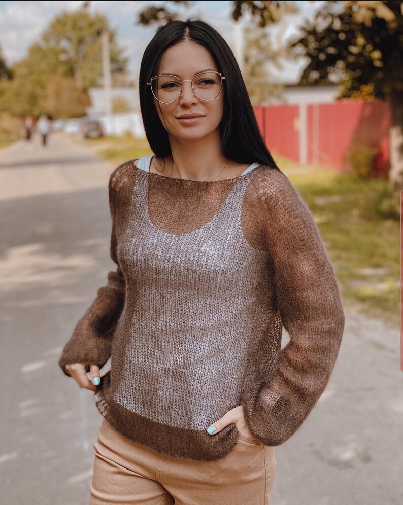 May include: A brown sheer knit sweater with long sleeves and a loose fit. The sweater has a subtle ombre effect, transitioning from a lighter brown at the top to a darker brown at the bottom.