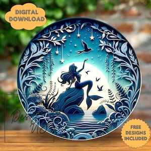 May include: A blue and white decorative plate featuring a mermaid sitting on a rock, reaching towards the sky. The plate has a layered design with stars, birds, and aquatic plants. The words "DIGITAL DOWNLOAD" and "FREE DESIGNS INCLUDED" are also visible.