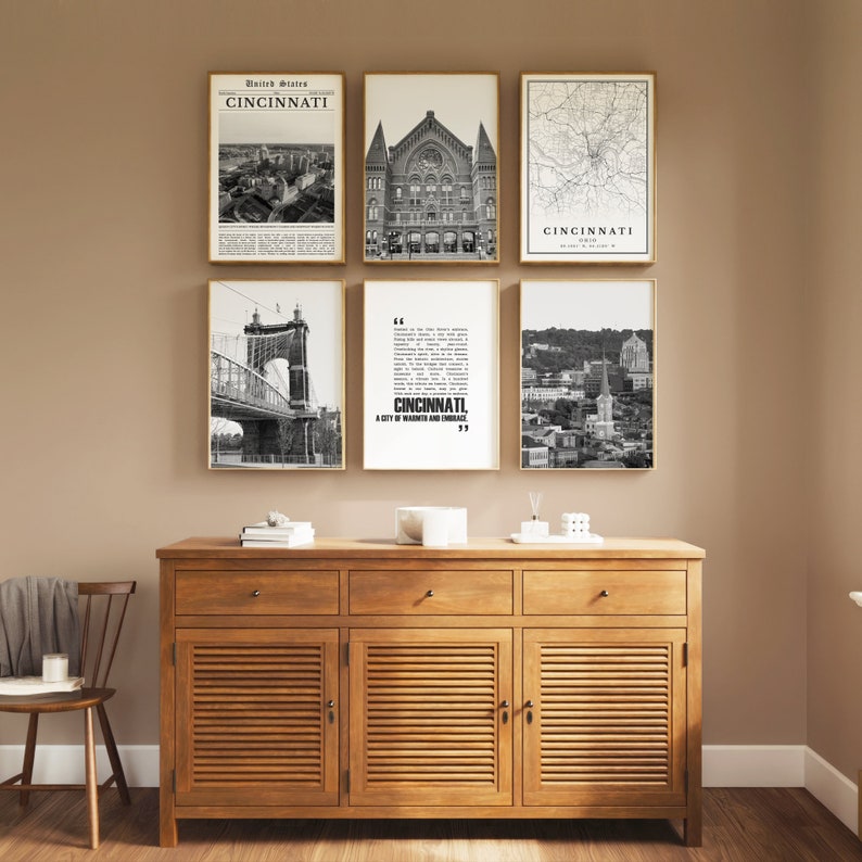 May include: A set of six black and white framed prints featuring images of Cincinnati, Ohio. The prints include a map of the city, a view of the city skyline, a bridge, and a building. The prints are arranged in a grid pattern on a wall above a wooden cabinet.