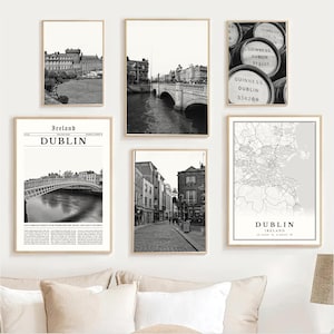 May include: A collection of framed black and white prints featuring Dublin, Ireland. The prints include cityscapes, bridges, street scenes, a map, and Guinness barrels. The prints are displayed on a white wall.