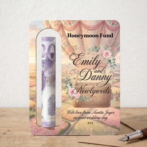May include: A decorative card with a slot holding a twenty-dollar bill. The card features a hot air balloon design with the words "Honeymoon Fund," "Emily and Danny Newlyweds," and a message from Auntie Joyce.