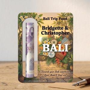 May include: A wooden Bali Trip Fund money box with a slot for inserting cash. The box features a tropical design with the names "Bridgette & Christopher" and the word "BALI". A rolled-up bill is visible through the slot.