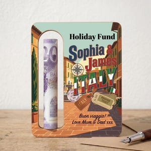 May include: A wooden money holder with a cutout for a twenty-dollar bill. The holder is decorated with a travel-themed design, including the words "Holiday Fund," "Sophia & James," and "Italy." The design also includes the text "Buon viaggio! Love Mum & Dad xxx."