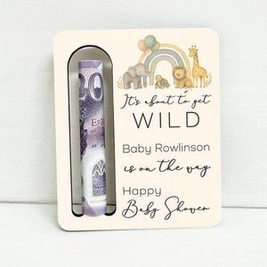 May include: A wooden baby shower gift card holder with a slot for cash. The card features a watercolor illustration of a rainbow, animals, and the text "It's about to get WILD" and "Baby Rowlinson is on the way."