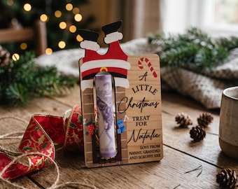 May include: A wooden Christmas money holder featuring a cutout of Santa's legs going down a chimney. The board displays the text A LITTLE Christmas TREAT FOR Natalie LOVE FROM NANNY, GRANDAD AND SCRUFFY XXX with a candy cane graphic.