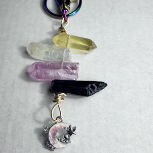 May include: A crystal keychain with a gold-toned metal ring, featuring a crescent moon charm with stars and four crystal points in shades of purple, green, and yellow.