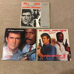 May include: Three VHS movie covers from the Lethal Weapon film series. The covers feature Mel Gibson and Danny Glover. The first cover is for Lethal Weapon, the second is for Lethal Weapon 2, and the third is for Lethal Weapon 3.