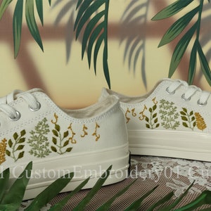 May include: White canvas sneakers with green and yellow embroidered floral designs. The shoes have white laces and a white rubber sole.