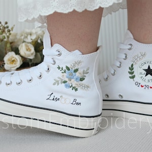 Może przedstawiać: Białe, wysokie trampki Converse z haftowanymi wzorami kwiatowymi i tekstem "Lise & Ben" na jednym bucie i "Converse All Star 01 &hearts; 19 &hearts; 25" na drugim.