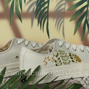 May include: White canvas sneakers with green and yellow embroidered floral designs. The shoes have white laces and a white rubber sole.