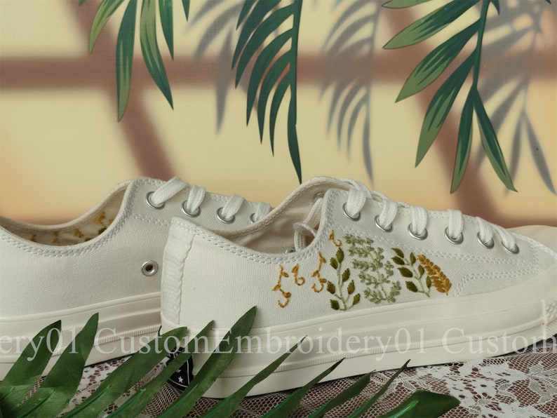 May include: White canvas sneakers with green and yellow embroidered floral designs. The shoes have white laces and a white rubber sole.