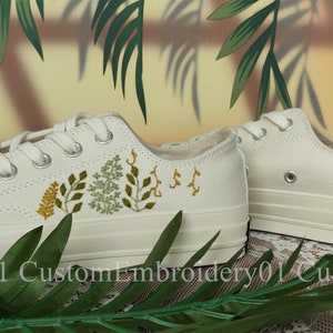 May include: White canvas low-top sneakers with green and yellow embroidered floral designs.