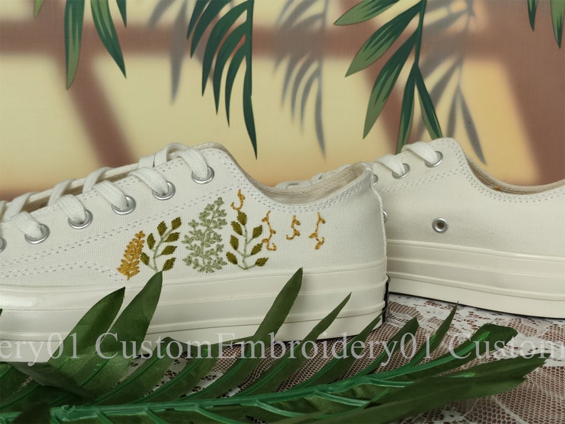May include: White canvas low-top sneakers with green and yellow embroidered floral designs.