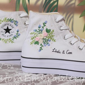 Puede incluir: Zapatillas Converse blancas de caña alta con diseños florales bordados y el texto "Linda & Cem" en una zapatilla.