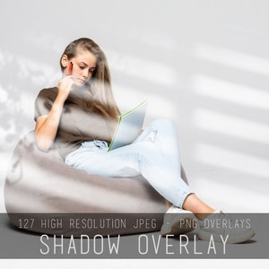 May include: A young person sits in a beanbag chair, reading a book and holding a pen. The background is a light gray wall with shadows from a window.