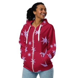 May include: A red zip-up hoodie with a pattern of light purple stars. The hoodie has a white zipper and white drawstrings. The person in the image is wearing blue jeans.