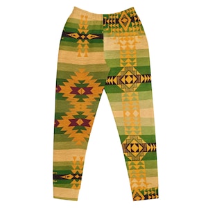 May include: Jogger pants with an all-over geometric pattern in shades of green, gold, and burgundy. The design features repeating diamond and triangle shapes, creating a Southwestern or tribal aesthetic. The pants have an elastic waistband.
