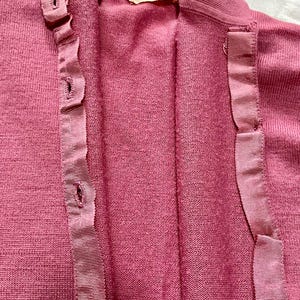 May include: A dusty rose knit cardigan featuring a button-down front with a matching grosgrain ribbon placket. The garment has a high collar and a Pendleton brand label at the inner neckline, displaying the text Pendleton and the number 40.