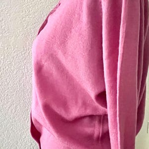 May include: A long-sleeved, solid pink knit sweater featuring a classic collar and a button-down front placket. The garment is crafted from a fine-gauge knit material and includes a ribbed hemline at the waist, displayed on a mannequin.