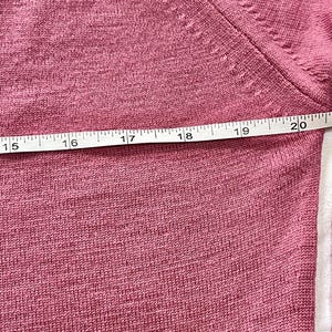 May include: A dusty rose knit sweater featuring a fine-gauge texture and a visible seam along the shoulder. A white measuring tape is positioned horizontally across the fabric, showing a measurement spanning from 15 to 20 inches in length.
