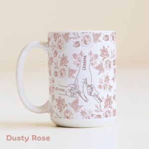 May include: White ceramic mug with a dusty rose floral pattern and a design of hands holding each other. The mug has the words "Grandma", "Olivia", and "Oliver" printed on it. The text "Dusty Rose" is at the bottom.