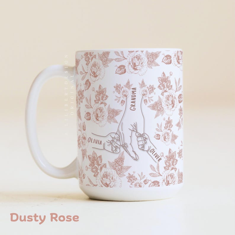 May include: White ceramic mug with a dusty rose floral pattern and a design of hands holding each other. The mug has the words "Grandma", "Olivia", and "Oliver" printed on it. The text "Dusty Rose" is at the bottom.