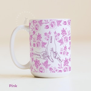 May include: White ceramic mug with a pink floral design. The mug features a graphic of hands holding each other, with the words "Mommy", "Sophia", and "Emily". The word "Pink" is at the bottom of the mug.