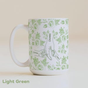 May include: White ceramic mug with a light green floral pattern and a graphic of hands holding each other. The mug has the words "Grammy", "Sophia", and "Emily" printed on it. The words "Light Green" are printed at the bottom.