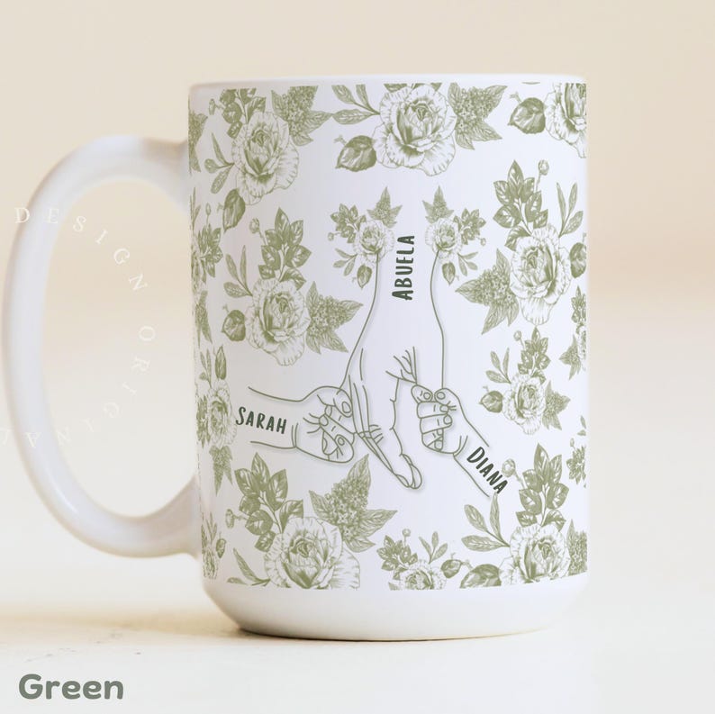 May include: White ceramic mug with a Dusty Rose floral pattern and a design of hands holding each other. The mug has the words "Grandma", "Olivia", and "Oliver" printed on it. The mug also has the words "Dusty Rose" printed on it.