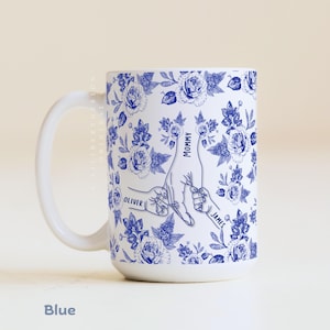 May include: White ceramic mug with a blue floral pattern and a design of hands holding each other. The mug has the words "Mommy", "Oliver", and "James" printed on it. The word "Blue" is at the bottom.