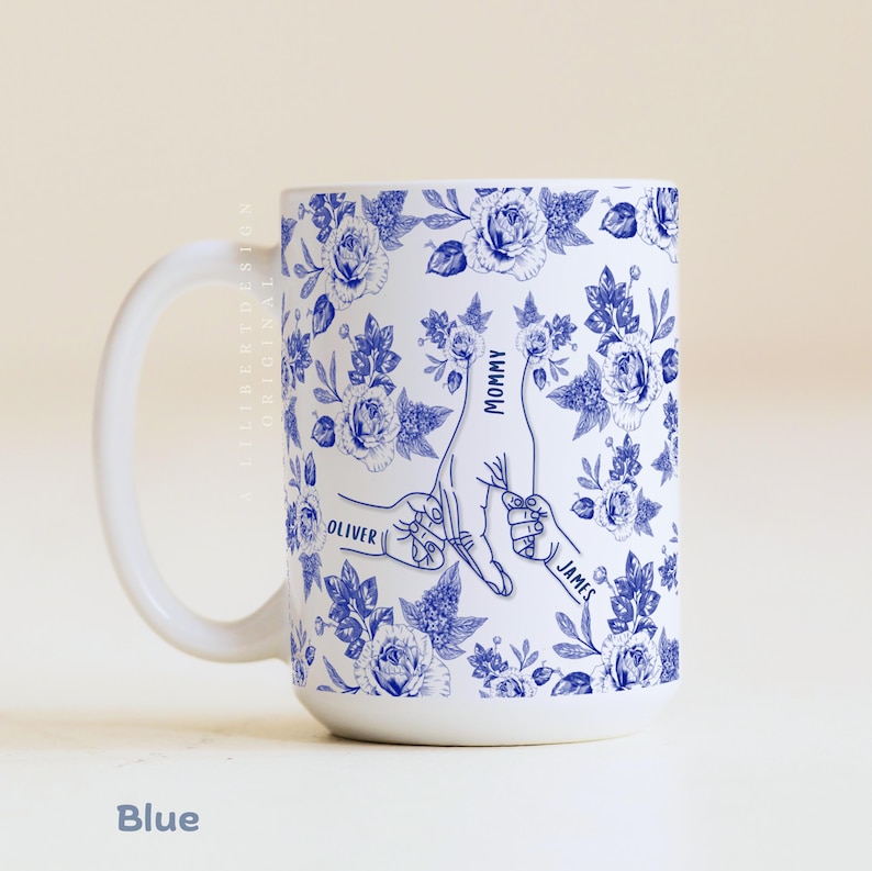 May include: White ceramic mug with a blue floral pattern and a design of hands holding each other. The mug has the words "Mommy", "Oliver", and "James" printed on it. The word "Blue" is at the bottom.