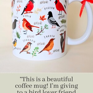 White ceramic coffee mug featuring colorful bird illustrations, including species like the Robin, Red Cardinal, Bullfinch,Sparrow, and Woodpecker. Each bird is labeled with its name, accompanied by small decorative musical notes and botanical details