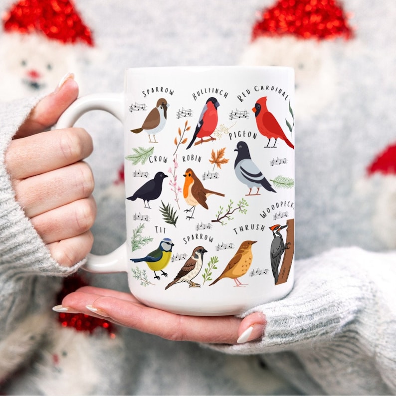 May include: White ceramic mug with a colorful illustration of different birds, including a sparrow, robin, bullfinch, red cardinal, pigeon, tit, thrush, and woodpecker. The birds are depicted with musical notes, suggesting a theme of bird songs.