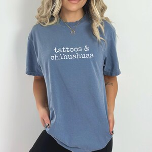 Op de afbeelding: Een blauw T-shirt met de tekst "tattoos & chihuahuas" in wit gedrukt op de voorkant.